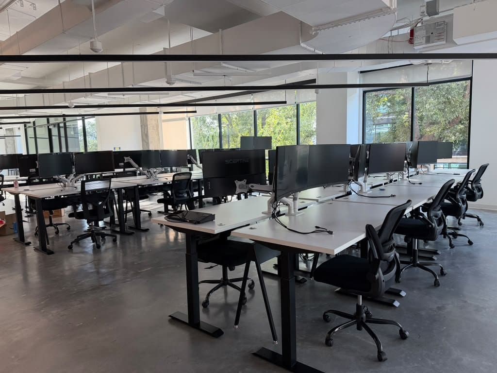 Open-plan Austin office with rows of height-adjustable desks on monitor arms, data and power runs dressed in