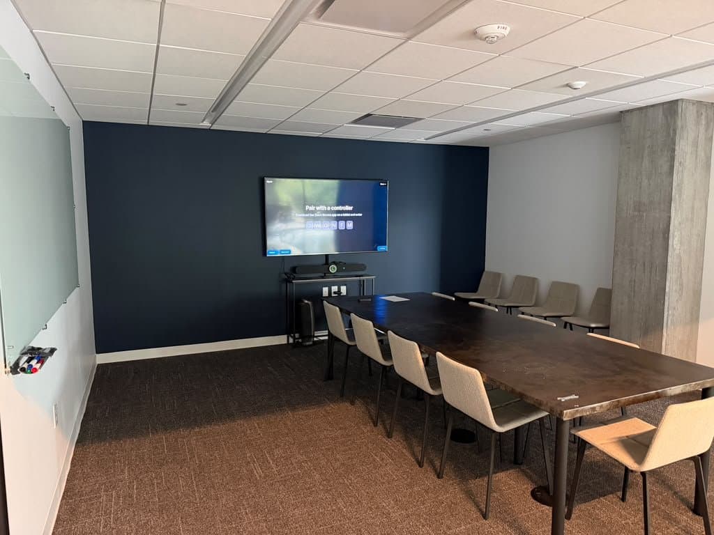 Conference room display and video bar mounted on a navy accent wall, cabling concealed behind the credenza