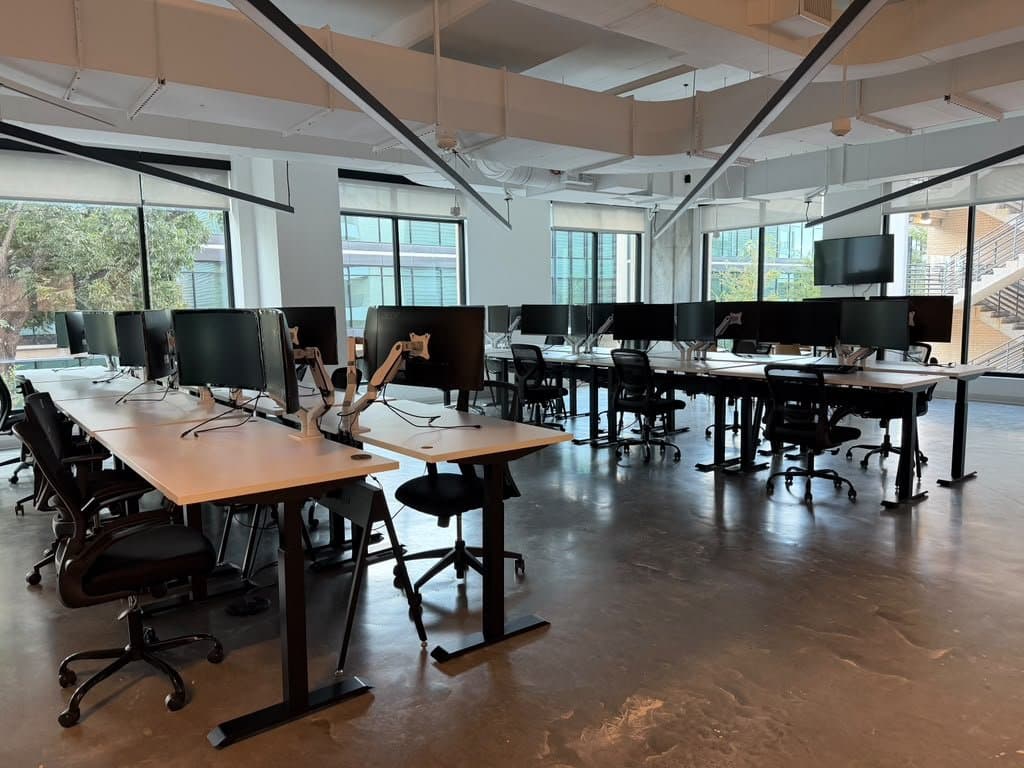 Second open-plan floor — desk rows wired for dual monitors, with a wall-mounted display at the end