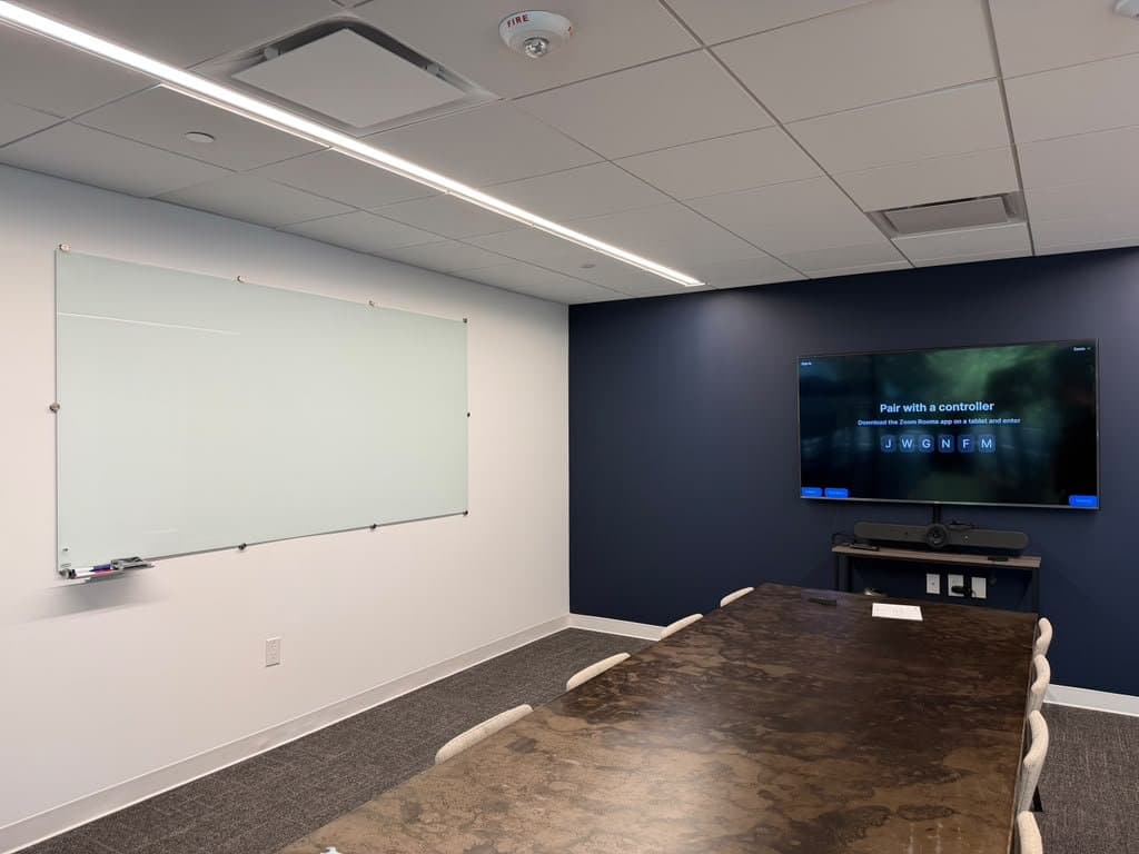 Conference room display and video bar on a navy accent wall, beside a glass whiteboard