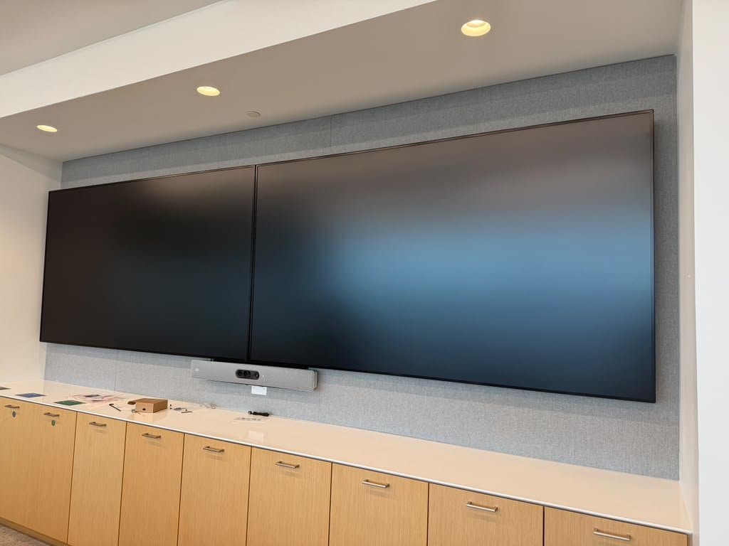 Two large displays side by side on an acoustic-fabric wall with a centre video bar