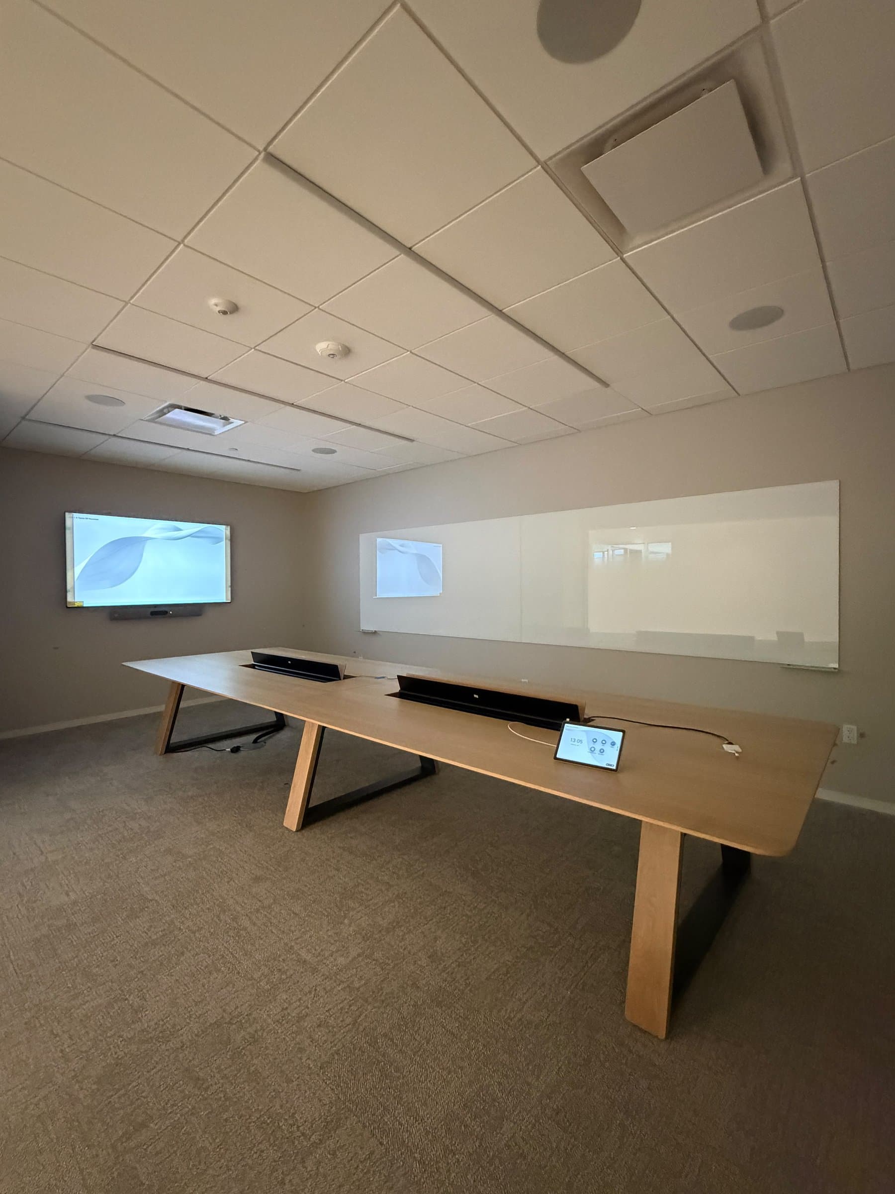 Boardroom with a display, in-ceiling speakers, table soundbars and a tabletop meeting controller