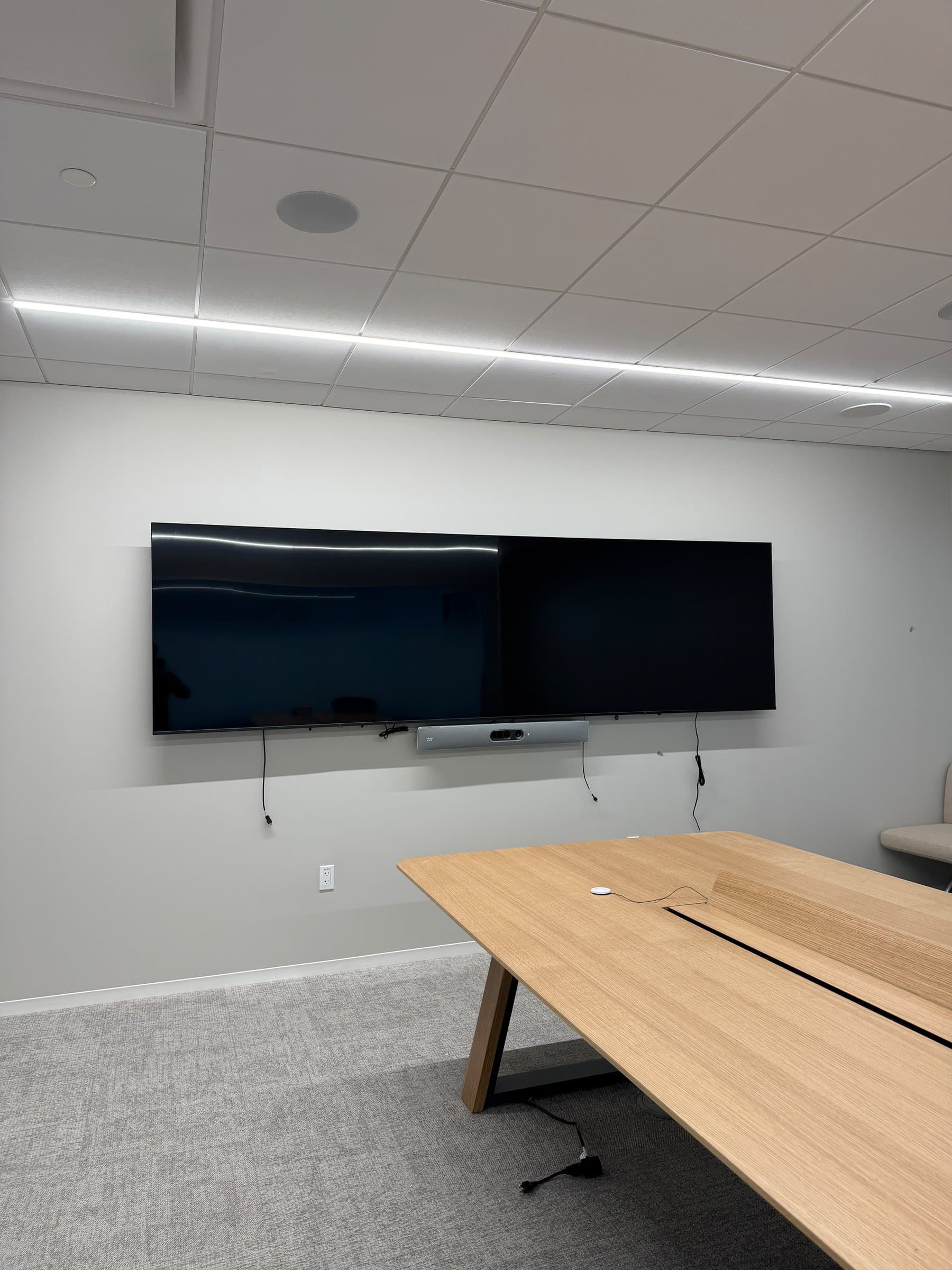 Dual displays on a wall rail with a video bar and in-ceiling speakers above the conference table