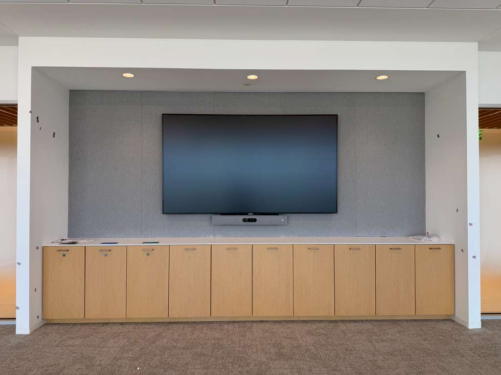 Boardroom display set into a grey acoustic-fabric wall above a full-length millwork credenza, video bar below