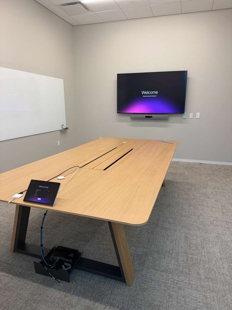 Meeting room display and video bar beside a glass whiteboard, with the table's floor box and data run dressed underneath