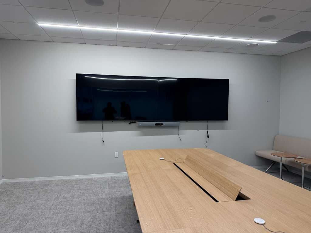 Conference room with two wide displays side by side and a centre video bar above a cable-managed meeting table