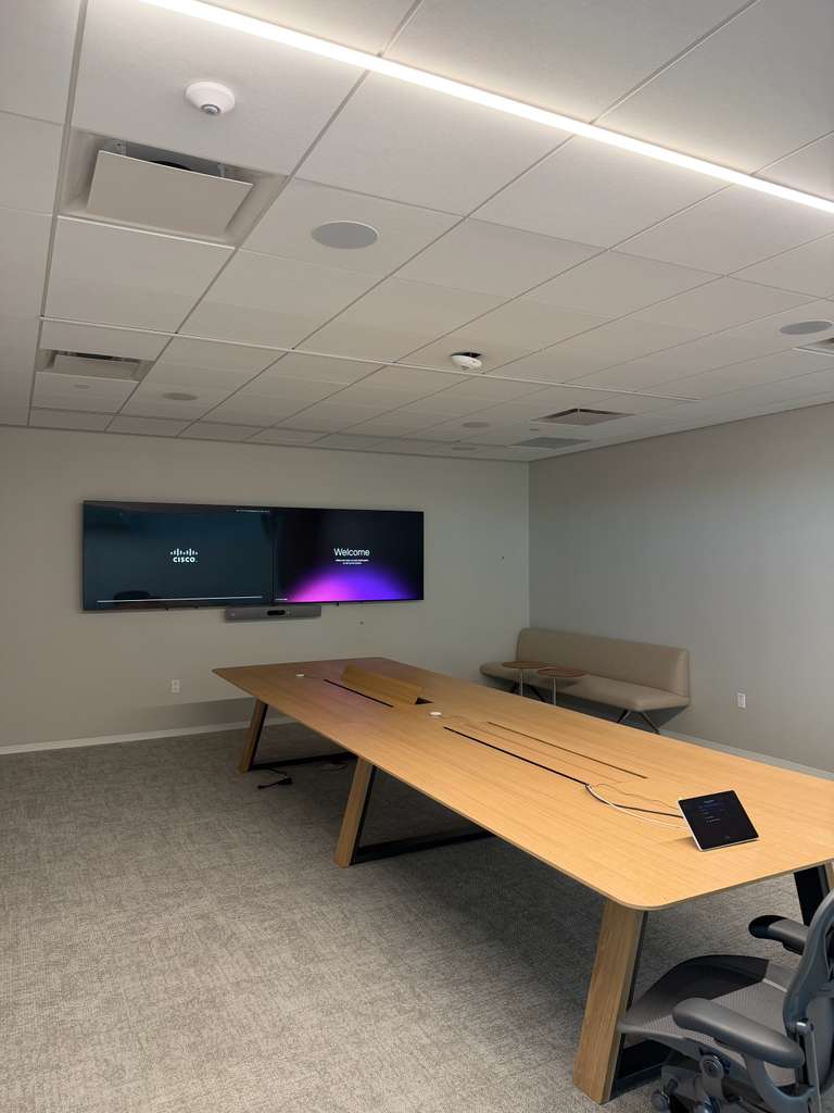 Dual conference displays with a video bar and in-ceiling speakers, powered up for the room's first call