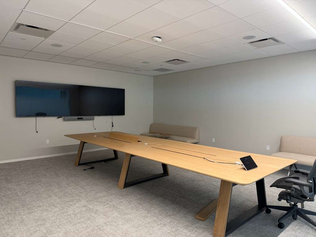 Long-table conference room with dual displays, a video bar and a tabletop controller, cabling routed out of sight