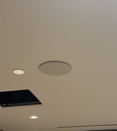 Flush in-ceiling speaker set into a smooth drywall ceiling between downlights