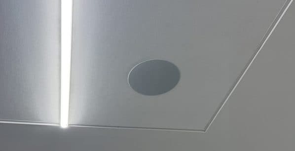 Flush ceiling speaker placed beside a recessed linear light in a drywall ceiling