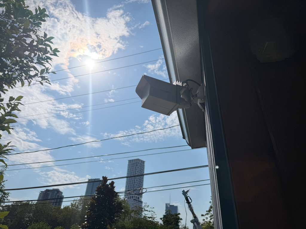 Point-to-point wireless bridge mounted on the corner of a dark metal building, aimed across the utility lines toward the Austin skyline