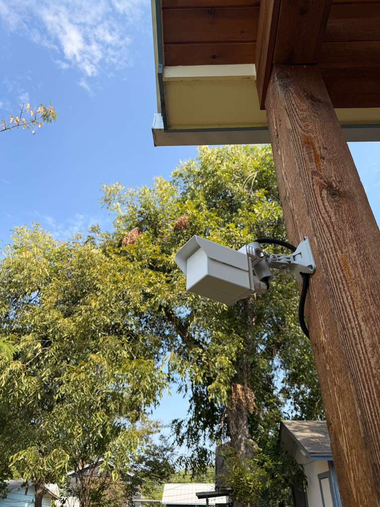 Point-to-point radio on an articulated bracket under a roof eave, with weatherproofed conduit down the post