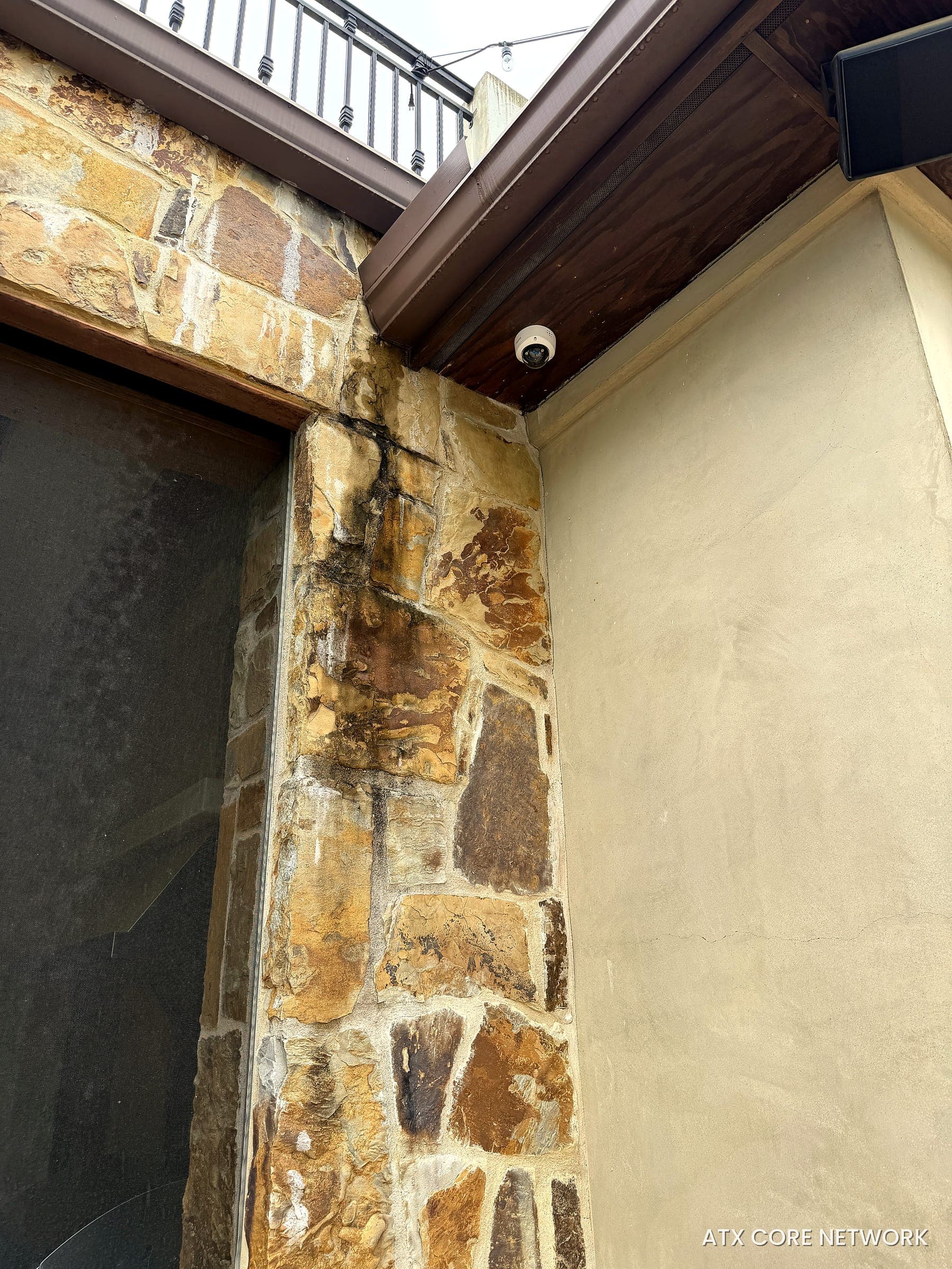 Dome IP camera installed under the wood soffit of a stone home