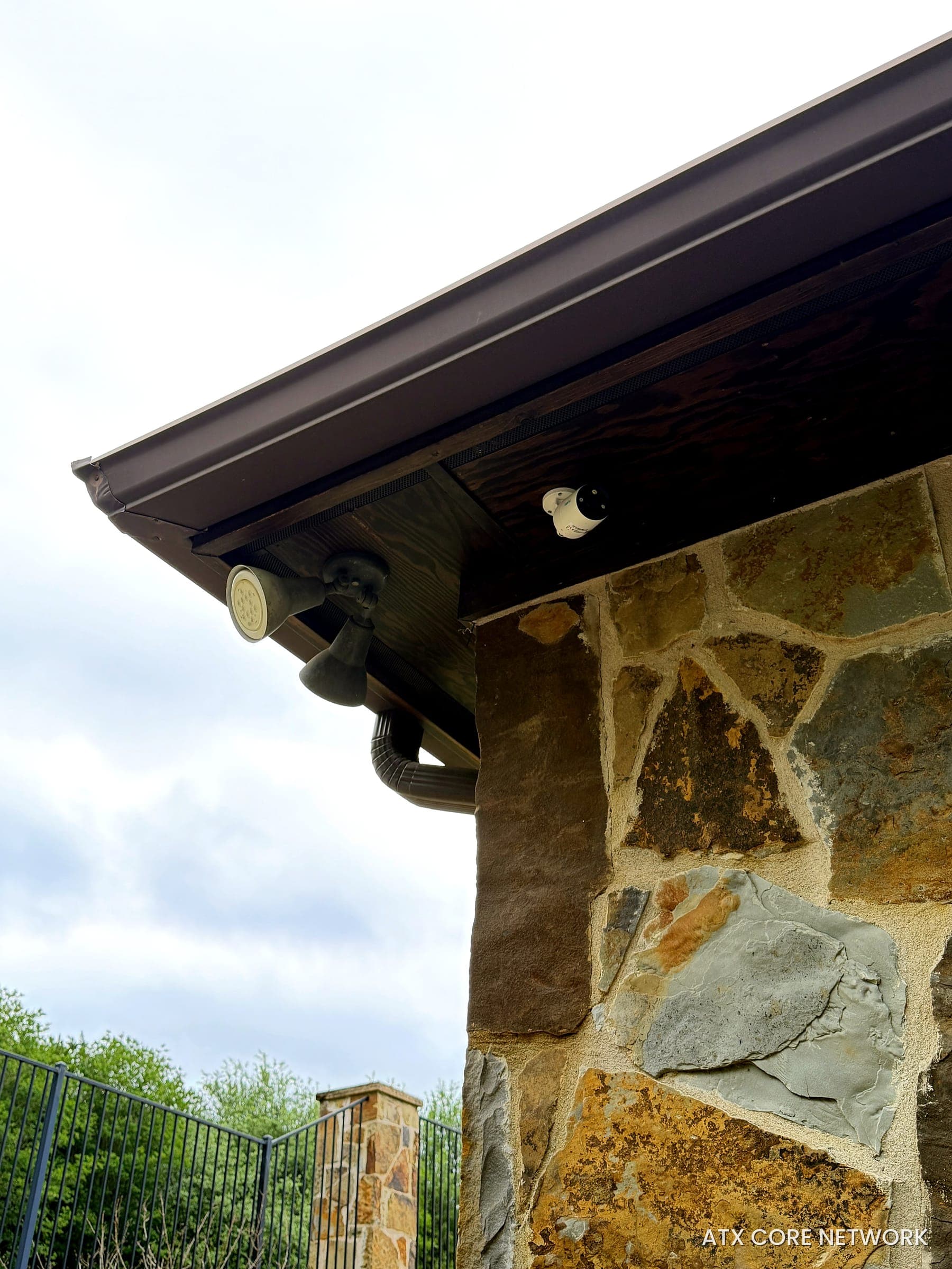 Bullet IP camera and landscape lighting under a stone home's eave