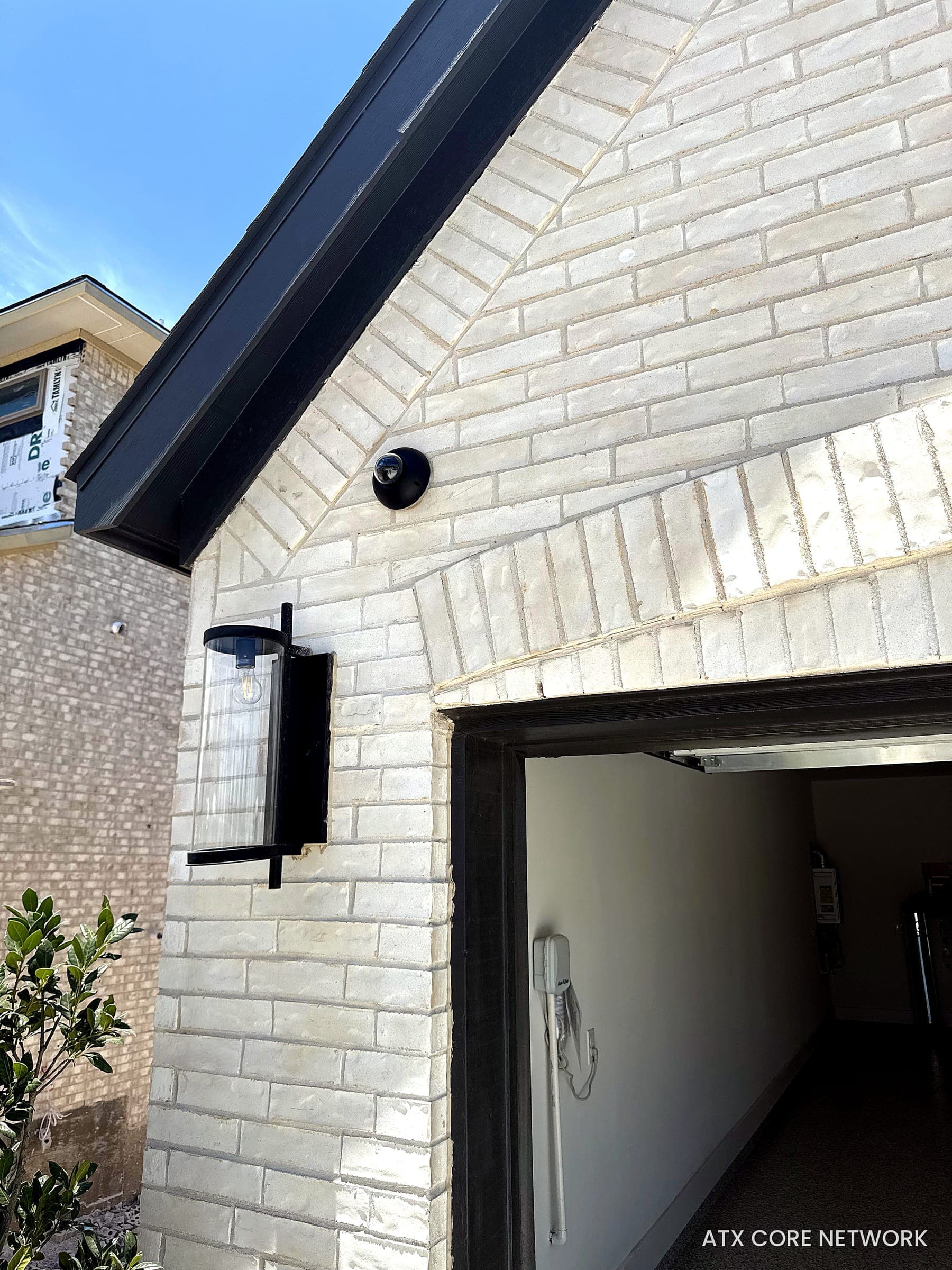 Black dome camera mounted on a white brick gable above a garage