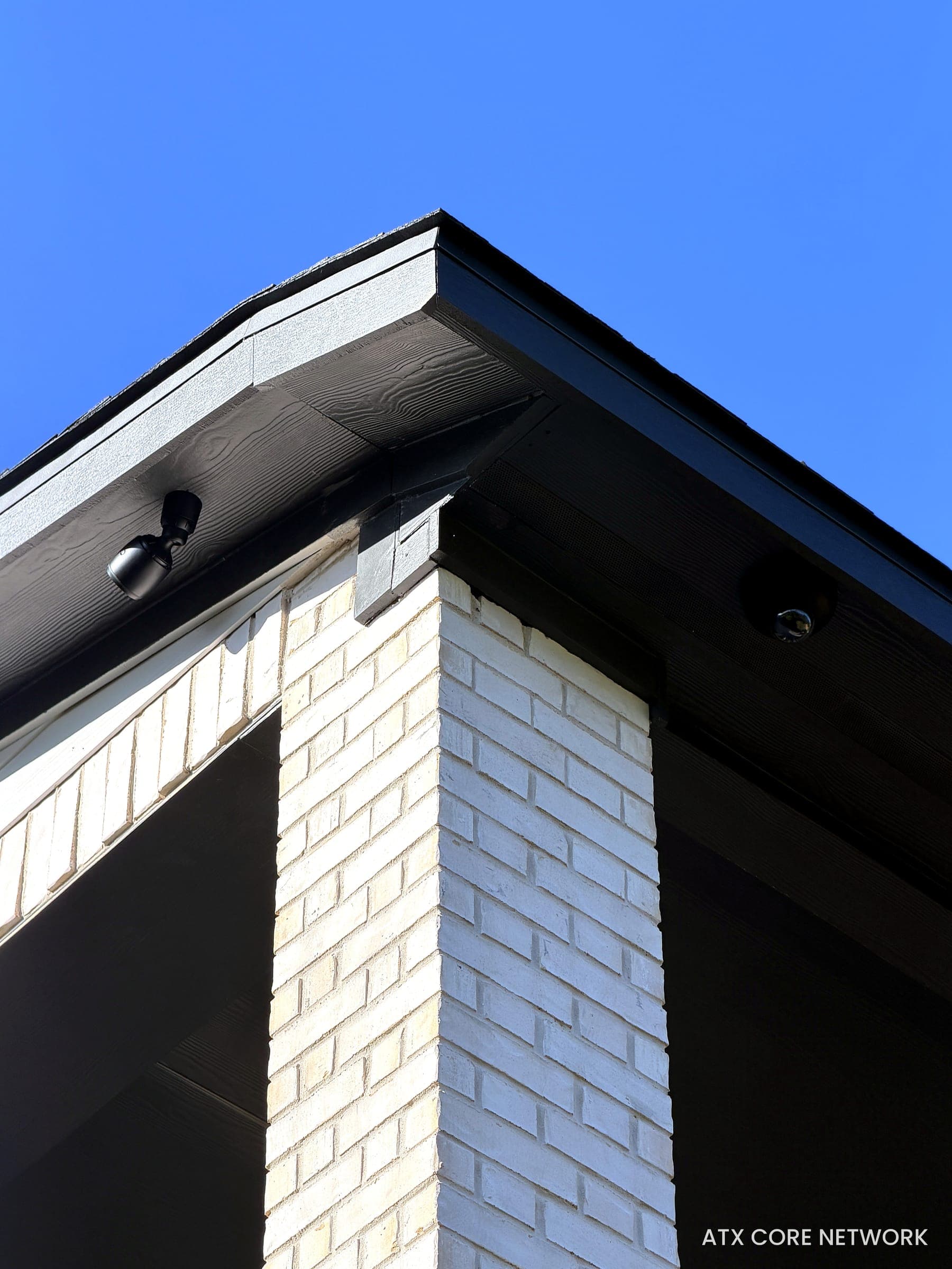 Two exterior IP cameras covering the corner of a white-brick home